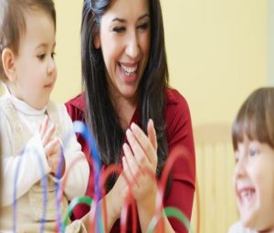 Young mother clapping and smiling as two toddlers play and laugh.